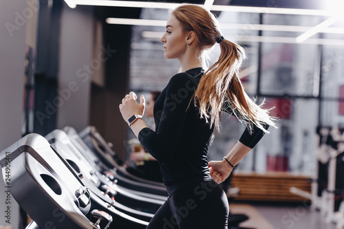 The athletic girl dressed in a black sportswear running on the treadmill in the modern gym