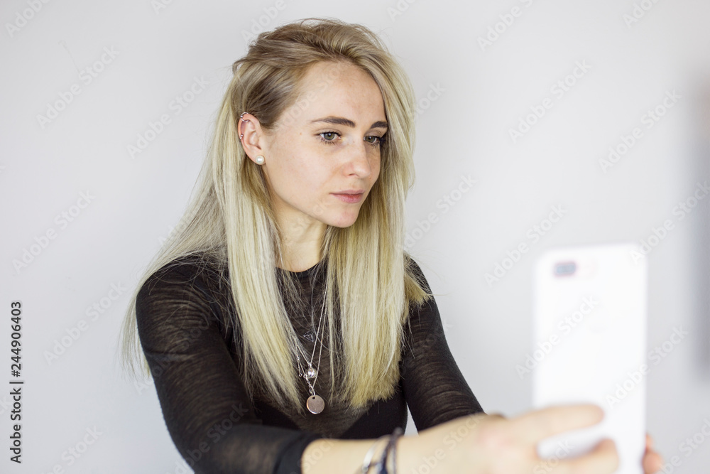 Naklejka premium Girl making selfie on smartphone, against a white wall