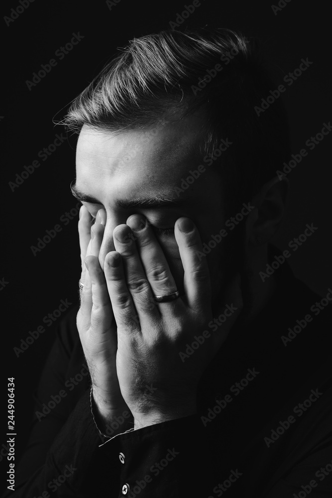 Black and white portrait of a stylish man with a beard and stylish hairdo dressed in the black shirt holding his hands on his face on the black background Black and white portrait of a stylish man with a beard and stylish hairdo dressed in the black shirt holding his hands on his face on the black background