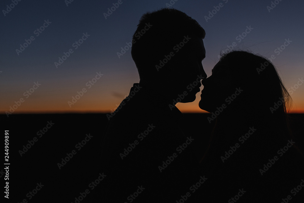 The silhouettes of the young man and woman in the sunset.