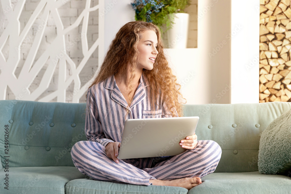 Portrait of pretty model working on notebook at home in cozy atmosphere. Adorable girl sitting with laptop on couch in pyjamas. Businesswoman job and morning concept Portrait of pretty model working on notebook at home in cozy atmosphere. Adorable girl sitting with laptop on couch in pyjamas. Businesswoman job and morning concept