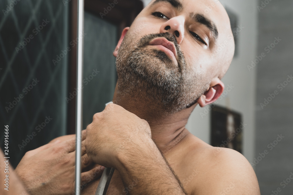 Fototapeta premium 40 year old British Asian male grooming - looking in the mirror - using a cut throat razor. 