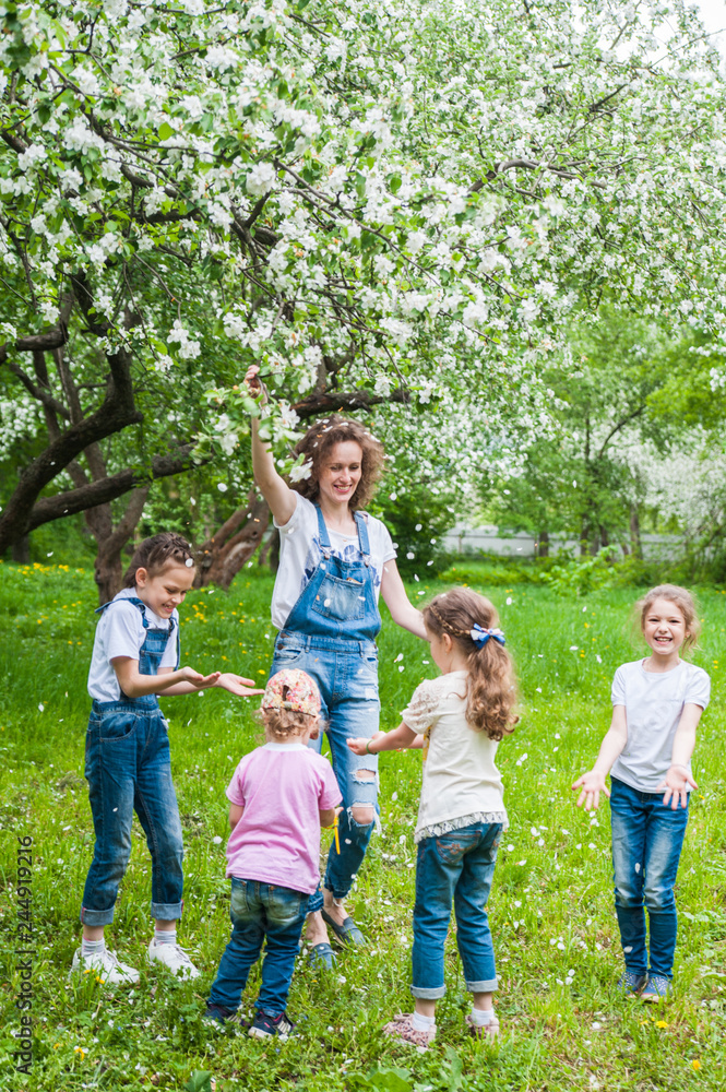 Obraz premium Woman and four little girls playing in blooming apple blossom garden.