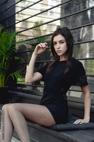 portrait of a young beautiful brunette woman on the street, model posing, women's urban street fashion, strict sexy black dress