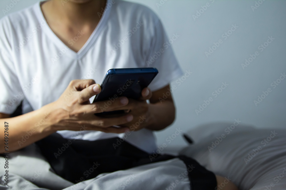 Young man sitting on the bed using smartphone at late night, Phone disease and Nomophobia. Healthy Concept Young man sitting on the bed using smartphone at late night, Phone disease and Nomophobia. Healthy Concept