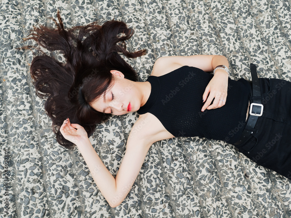 Naklejka premium High angle view of a pretty woman with black long hair in black dress lying on the ground with eyes closed, portrait of romantic young female has a good dream. 