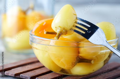 Pickled preserved bell peppers in glass bowl on wooden background