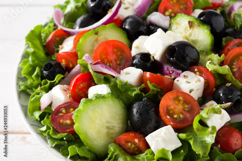 Fresh Greek salad in bowl with black olive,tomato,feta cheese, cucumber and onion on white wooden table. Close up