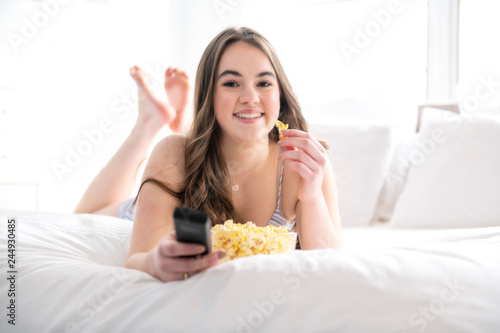 A young teenager watching movies in bed with popcorn