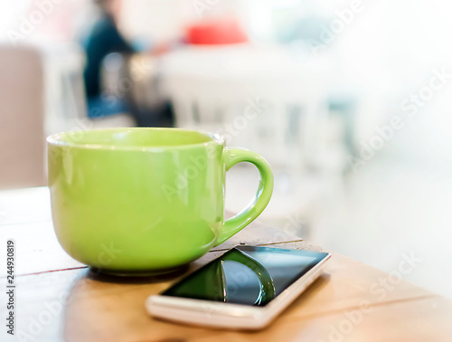 A big green mug with a drink and a smartphone on a wooden table in a cafe