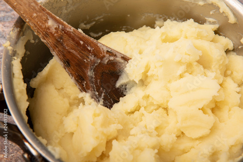 Close up image of a pan of mashed potato with a wooden spoon 