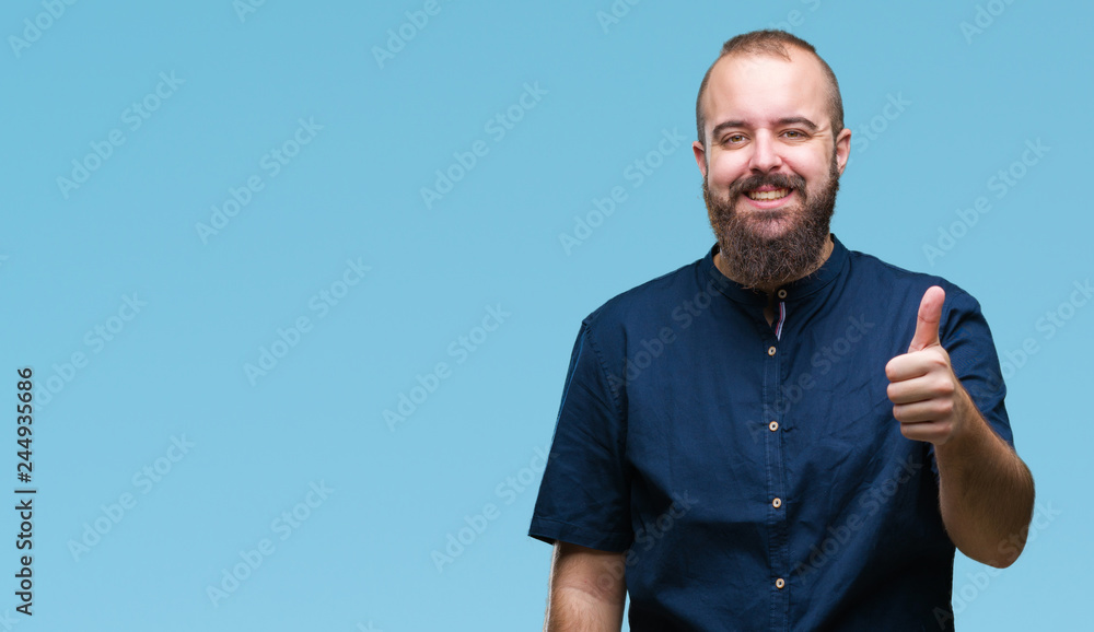 Young caucasian hipster man over isolated background doing happy thumbs up gesture with hand. Approving expression looking at the camera with showing success. Young caucasian hipster man over isolated background doing happy thumbs up gesture with hand. Approving expression looking at the camera with showing success.