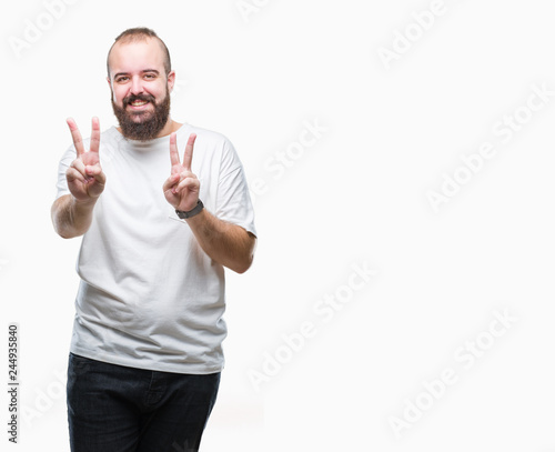 Young caucasian hipster man wearing casual t-shirt over isolated background smiling looking to the camera showing fingers doing victory sign. Number two.