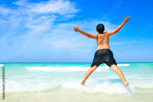 The boy took off his shirt and made a jump. Come to play the beautiful sea, white sand beach, clear water.