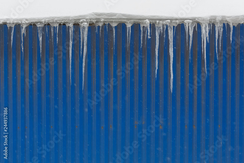 Icicles hanging from roof of the building opposite the blue wall  copy space fall icicles    old winter  poor thermal insulation  ice stalactite  formation of icicles  frost and winter weather concept.