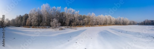 Rime and hoarfrost covering trees. Aerial view of the snow-covered forest and lake from above. Winter scenery. Landscape photo captured with drone. © Curioso.Photography