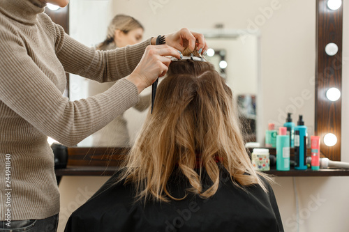 process of hair styling in the hairdressing salon. Professional hairdresser working with client in salon Hairstyle master makes an evening hairstyle flat hair in the hands of hairdresser