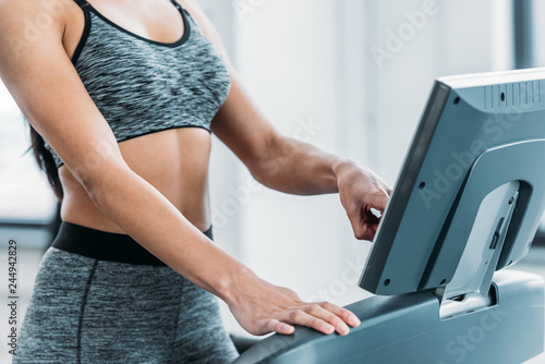 cropped shot of african american girl in sportswear training on treadmill in gym