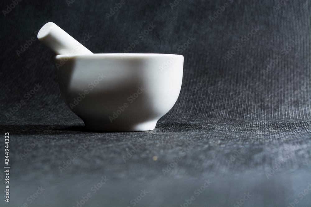 White mortar with a pestle from porcelain. A drinking bowl for crushing of spices. Black background. Kitchen utensils. Ware.