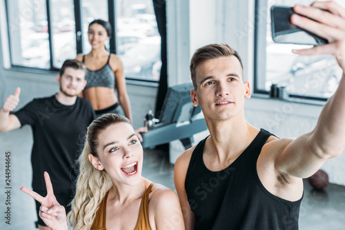 multiethnic group of sportive young friends taking selfie with smartphone in gym