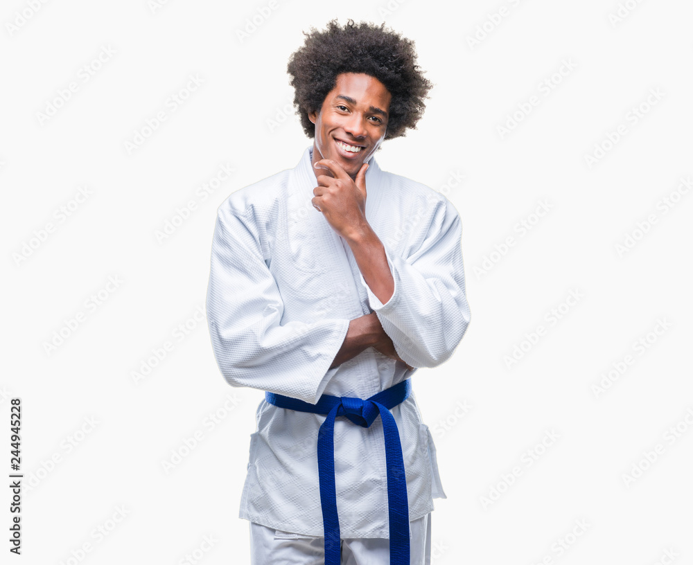 Afro american man wearing karate kimono over isolated background looking confident at the camera with smile with crossed arms and hand raised on chin. Thinking positive. Afro american man wearing karate kimono over isolated background looking confident at the camera with smile with crossed arms and hand raised on chin. Thinking positive.