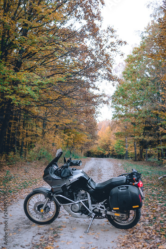 Adventure motorcycle standing on the road yellow forest tree on background, autmn season, vertical photo