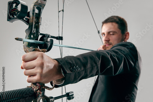 Businessman aiming at target with bow and arrow isolated on gray studio background. The business, goal, challenge, competition, achievement, purpose, victory, win, clarity, winner and success concept