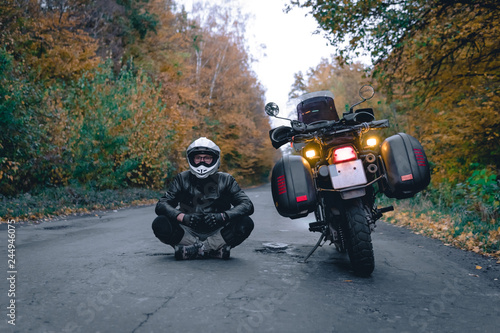 Biker man in leather jacket and black tourist motorcycle with side bags. wallpaper concept  enduro advetnture  space for text  autmn season  problems on the road accident