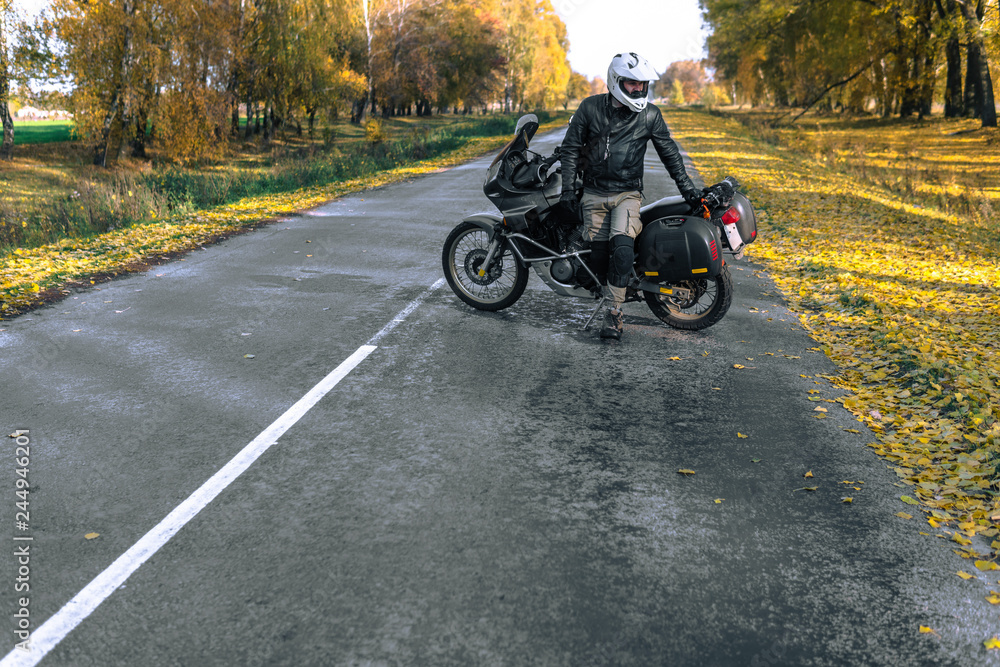 Fototapeta premium Rowerzysta mężczyzna w skórzanej kurtce i czarny motocykl turystyczny z bocznymi torbami. koncepcja tapety, reklama enduro, miejsce na tekst, sezon świąteczny
