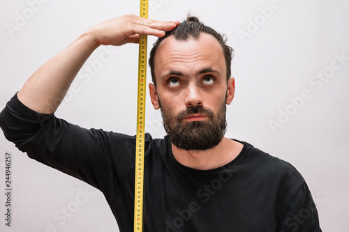 a man with a beard and a black t-shirt makes measurements of his height with a tape measure photo