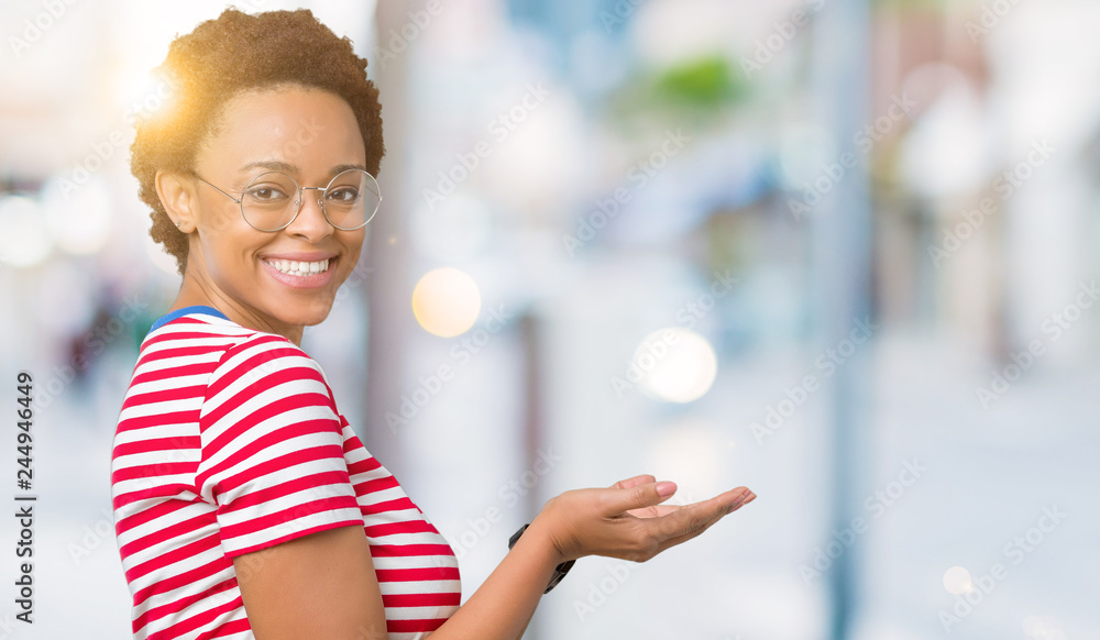 Beautiful young african american woman wearing glasses over isolated background Pointing to the side with hand and open palm, presenting ad smiling happy and confident Beautiful young african american woman wearing glasses over isolated background Pointing to the side with hand and open palm, presenting ad smiling happy and confident