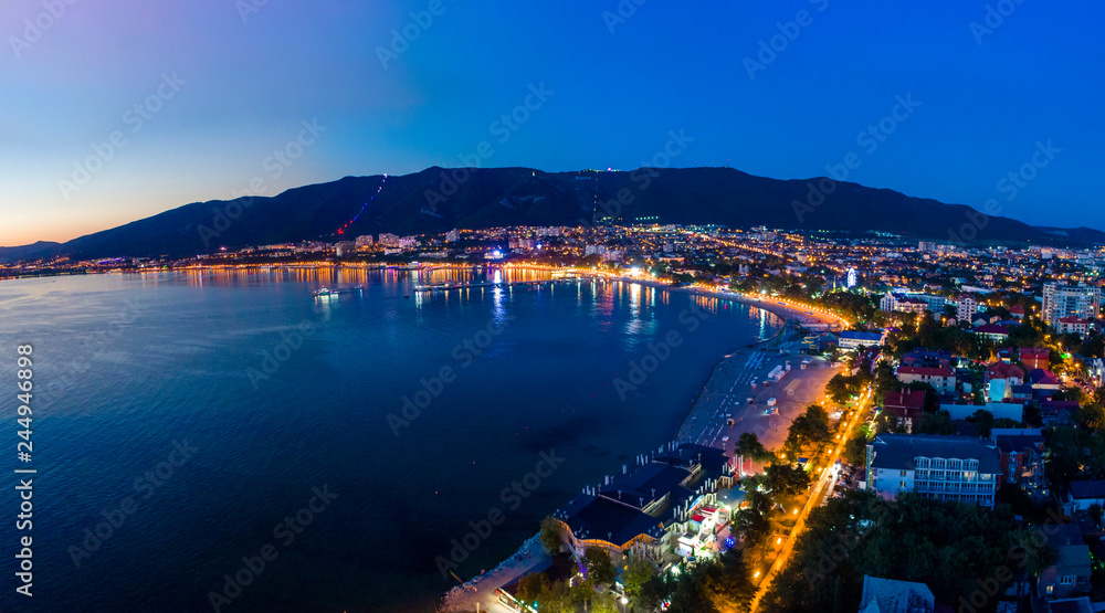 Gelendzhik embankment in the evening twilight from a bird's-eye view. The lights of the promenade are reflected in the smooth water of the Bay. Visible buildings of hotels and boarding houses. 