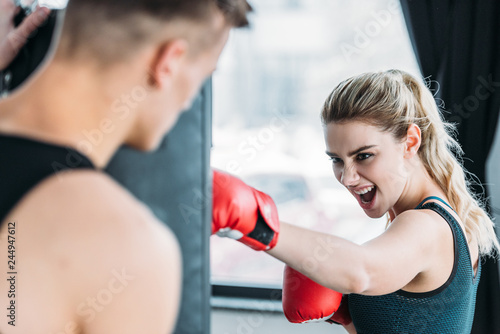 selective focus of male trainer looking at aggressive sportswoman boxing with punching bag in gym © LIGHTFIELD STUDIOS