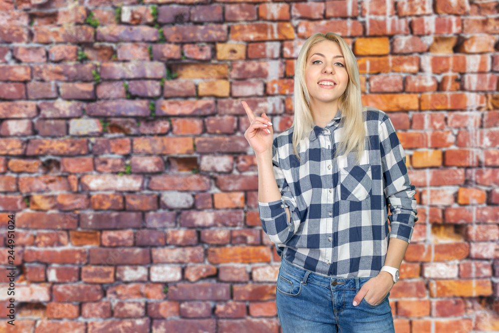 Young woman looking up and pointing at blank wall Young woman looking up and pointing at blank wall