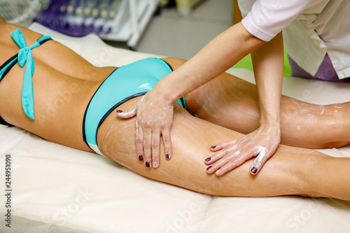 Masseur applying cream to woman's thigh. Massage in spa salon