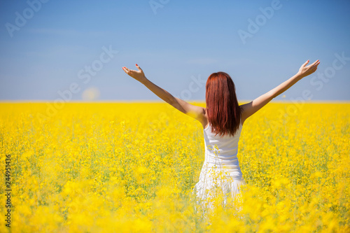 People freedom success concept. Happy woman in the field with flowers at sunny day in the countryside. Nature beauty background, blue sky and yellow flowers. Outdoor lifestyle.