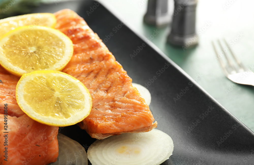 Pieces of tasty grilled salmon with lemon and onion on plate, closeup Pieces of tasty grilled salmon with lemon and onion on plate, closeup