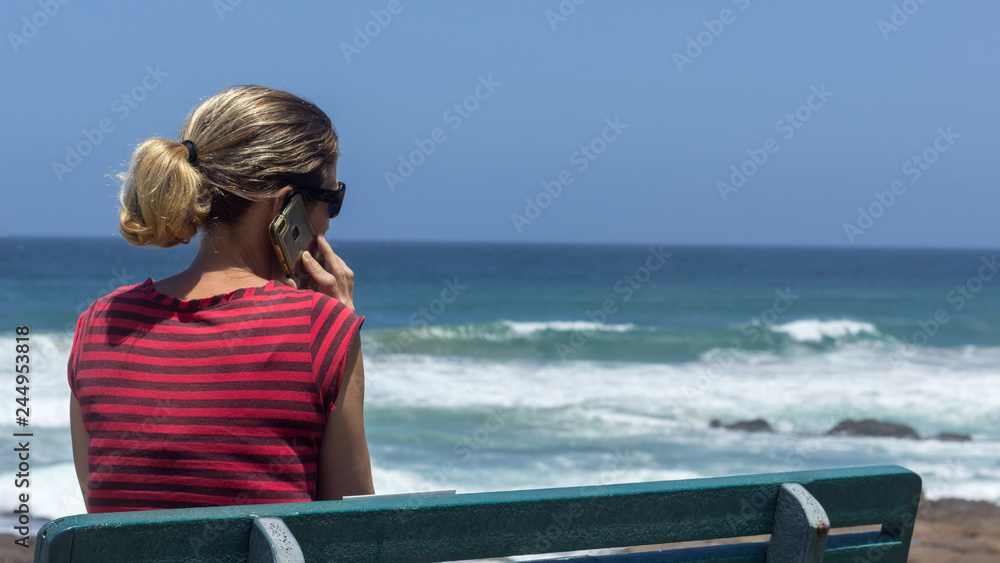 Fototapeta premium young healthy woman looking out to sea and talking on a cell phone