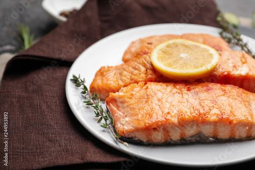 Pieces of tasty grilled salmon with lemon on plate, closeup