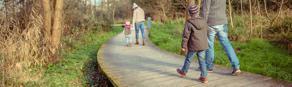 Back view of family walking together holding hands over a wooden pathway into the forest