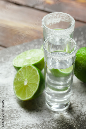 Tequila silver shots with lime slices and salt on wooden board