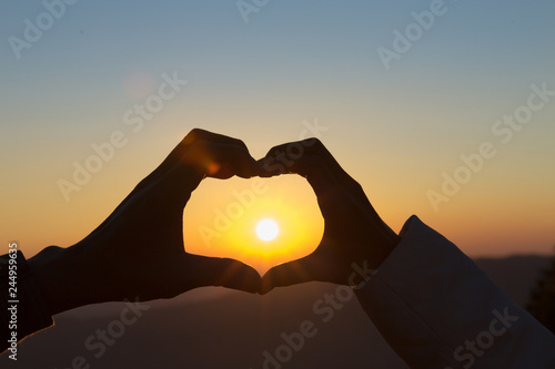 Closeup of couple making heart shape with hands and sunrise background, Happy in love.