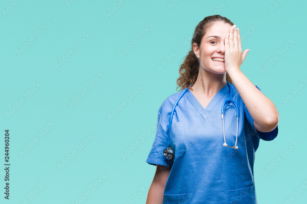 Young brunette doctor girl wearing nurse or surgeon uniform over isolated background covering one eye with hand with confident smile on face and surprise emotion. Young brunette doctor girl wearing nurse or surgeon uniform over isolated background covering one eye with hand with confident smile on face and surprise emotion.