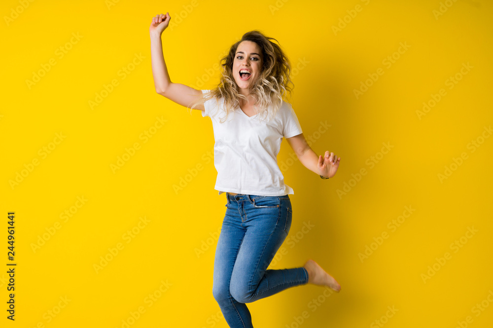 Beautiful young blonde woman jumping happy and excited over isolated yellow background Beautiful young blonde woman jumping happy and excited over isolated yellow background