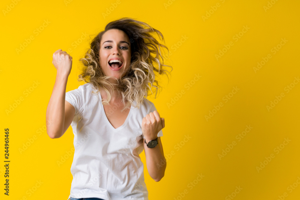 Beautiful young blonde woman jumping happy and celebrating with raised hands and open mouth over isolated yellow background Beautiful young blonde woman jumping happy and celebrating with raised hands and open mouth over isolated yellow background