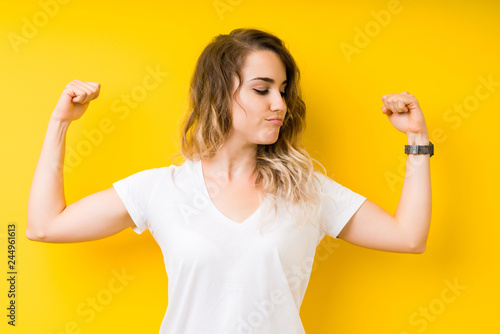 Young beautiful blonde woman over yellow background showing arms muscles smiling proud. Fitness concept.
