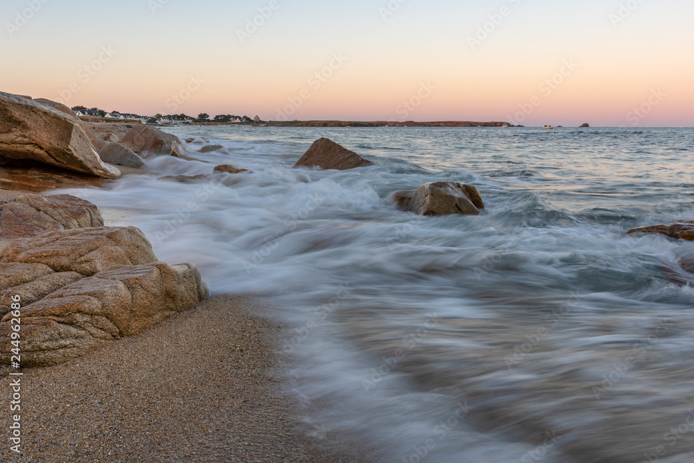 French landscape - Bretagne. A beautiful beach with rocks and port in the background at sunrise.