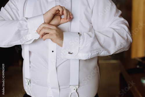 the groom fastens the sleeves on the shirt