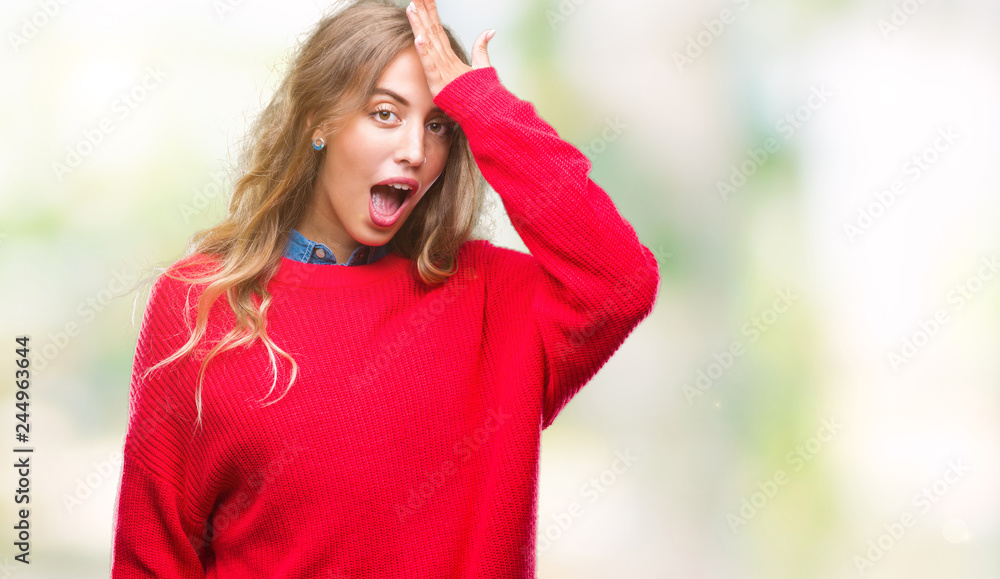 Beautiful young blonde woman wearing winter sweater over isolated background surprised with hand on head for mistake, remember error. Forgot, bad memory concept.