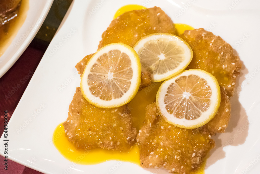 Close up view of lemon chicken with sauce and slice lemons on top in white plate Close up view of lemon chicken with sauce and slice lemons on top in white plate